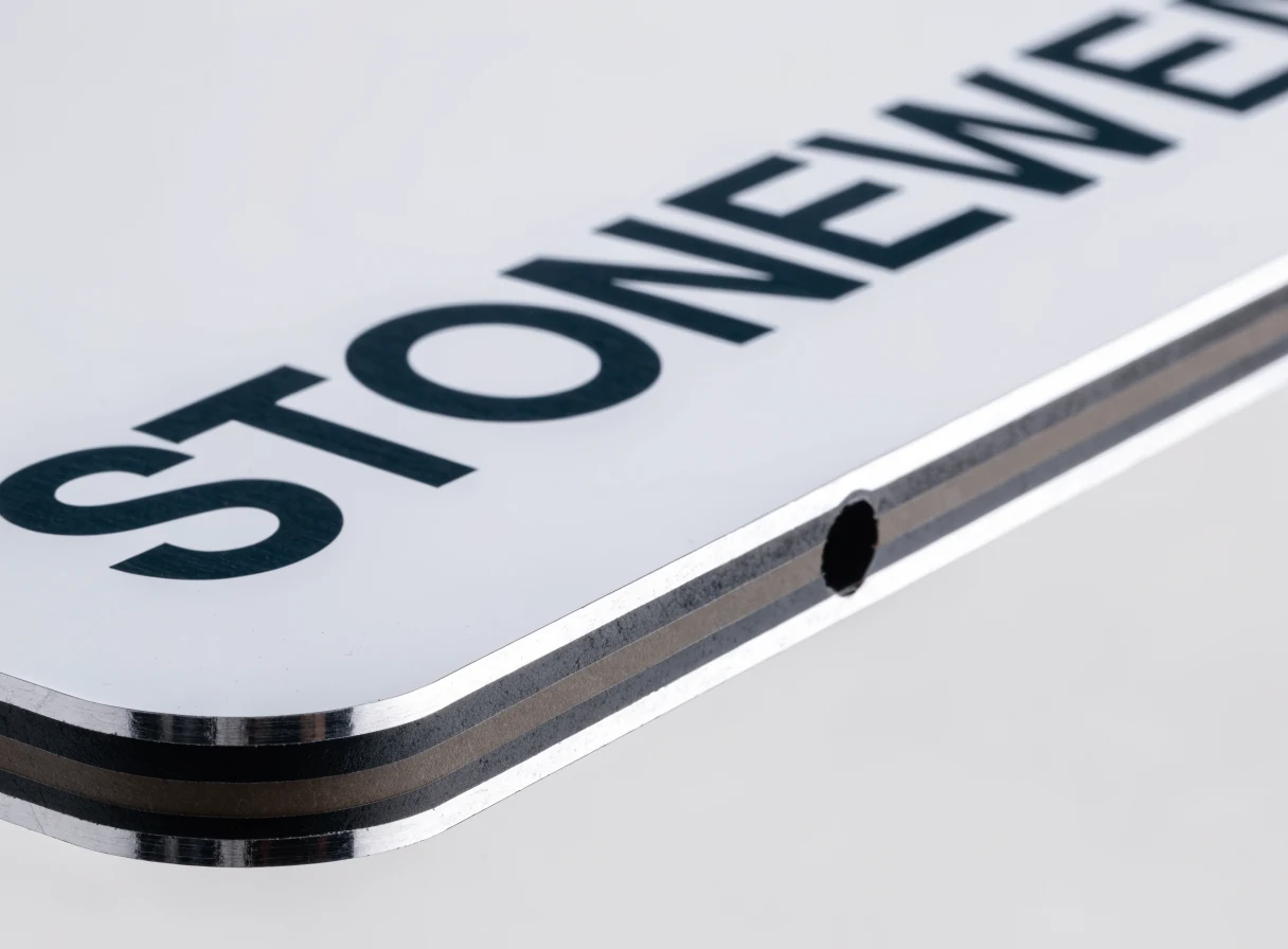 Cut edge of an aluminium composite panel showing both aluminium skins over the core, with a rounded corner and a punched mounting hole
